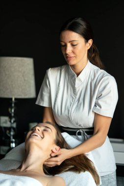 Masör spa salonunda genç kadın vücuduna masaj yapıyor.