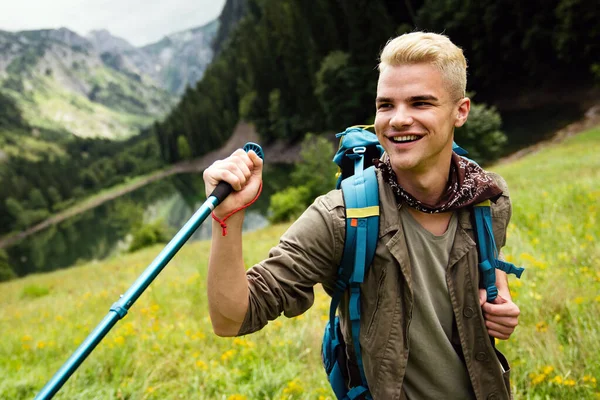 Hiker man with backpack and trekking poles looking at the mountains in outdoor