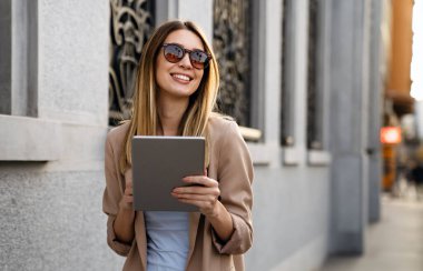 Çekici genç ve başarılı kadın kahve içiyor ve tatilin tadını çıkarırken dijital tablet kullanıyor.