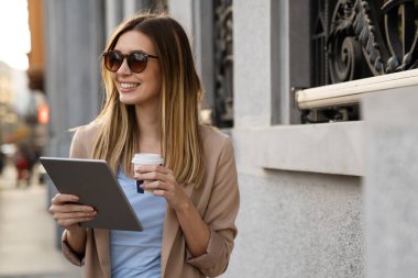 Dijital tablet kullanan başarılı bir genç kadının portresi kentsel arkaplanda kısa bir mola sırasında