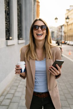 Çekici, genç ve başarılı bir kadın kahve içiyor ve molanın keyfini çıkarırken akıllı telefon kullanıyor.