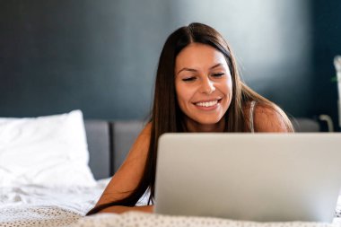 Mutlu genç bir kadın çalışıyor, evde dizüstü bilgisayarla web sörfü yapıyor. İnsanlar, teknoloji, ev kavramı