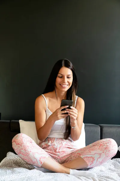 Aantrekkelijke Glimlachende Vrouw Met Behulp Van Smartphone Terwijl Ontspannen Thuis — Stockfoto