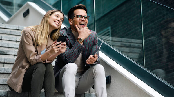 Young businessman and businesswoman discussing working together in urban background outdoors.