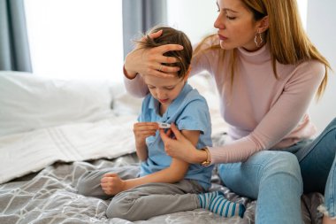 Anne hasta çocuğunun ateşini ölçüyor. Yüksek ateşi olan hasta bir çocuk ve annesi termometreyi tutuyor.