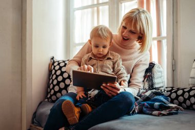 Mutlu aile teknolojisi konsepti. Gülümseyen anne ve küçük oğlu evde dijital tabletle oynuyorlar.