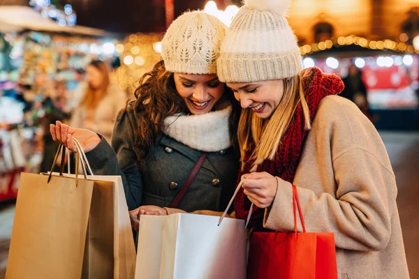 Noel indirimi ve insanlar konsepti. Alışveriş çantalı mutlu genç bayan arkadaşlar Noel pazarında alışveriş yapıyorlar.