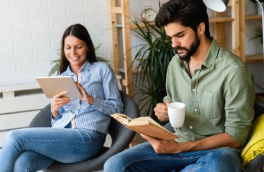 Mutlu genç çift evde dinleniyor. Kitap ve tablet bilgisayarda bir şeyler okunuyor.