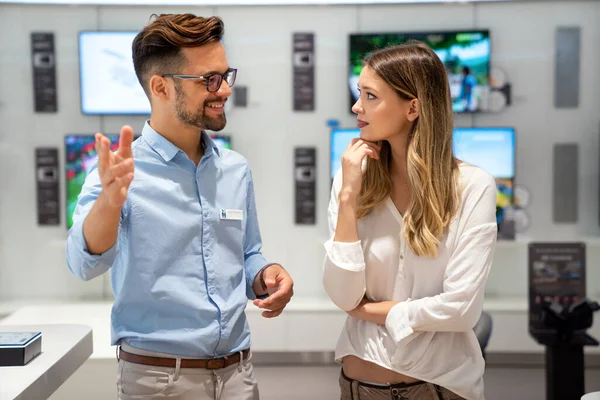 Tüketici elektroniği mağazasında yeni dijital cihaza bakan mutlu gençler