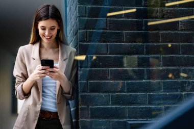 Şehir arka planında cep telefonu olan başarılı bir kadının portresi. İş teknolojisi aygıtı kavramı