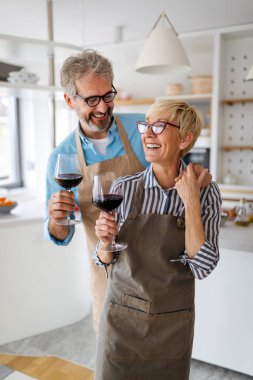 Mutlu son sınıf çifti ev mutfağında eğleniyor, yemek yapıyor ve şarap içiyor.