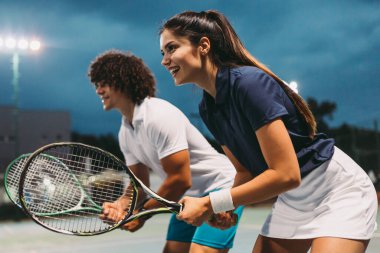 Tenis sporu insanları konsepti. Karışık genç çiftler oyuncusu tenis topuna vuruyor ve partner kalenin yanında duruyor