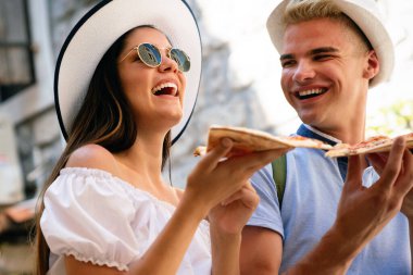 Yaz tatilinde sokakta pizza yiyen mutlu bir çift.