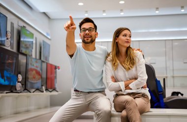 Tüketici elektroniği mağazasında yeni dijital cihaza bakan mutlu gençler