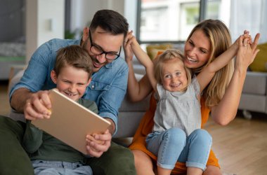 Mutlu genç aile evde eğleniyor. Çocuklu aileler tablet kullanıyor. İnsanlar mutluluk kavramını sever.