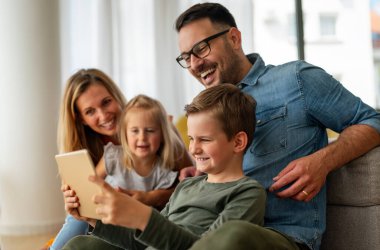 Mutlu genç aile evde eğleniyor. Çocuklu aileler dijital cihaz kullanıyor. Eğitim ebeveynliği mutluluk kavramı.