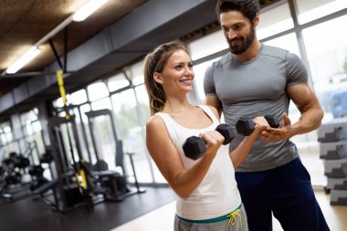 Spor salonunda halterlerle egzersiz yapan spor salonundaki spor hocasıyla mutlu bir kadın. Spor insanları spor konsepti