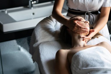 Masör spa salonunda genç kadın vücuduna masaj yapıyor.