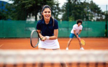 Tenis sporu insanları konsepti. Karışık genç çiftler oyuncusu tenis topuna vuruyor ve partner kalenin yanında duruyor