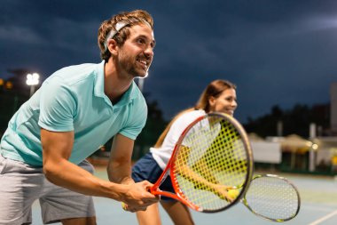 Tenis sporu insanları konsepti. Karışık genç çiftler oyuncusu tenis topuna vuruyor ve partner kalenin yanında duruyor