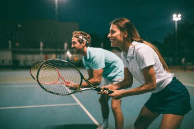 Tenis sporu insanları konsepti. Karışık genç çiftler oyuncusu tenis topuna vuruyor ve partner kalenin yanında duruyor