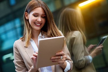Ofis binasında pencerelerin önünde dikilirken dijital tablet kullanan çekici genç bir iş kadını.