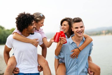 Mutlu arkadaşlar grubu plaj partisinde gün batımında kokteyl içerek eğleniyor. Tatildeki gençlerle yaz neşesi ve arkadaşlık konsepti