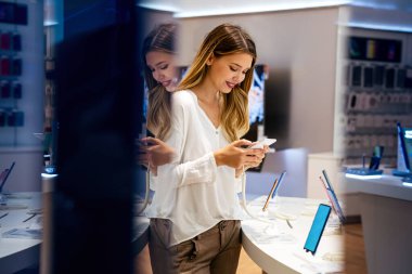 Alet dükkanından akıllı telefon alan mutlu genç bir kadının portresi. Yeni bir dijital aygıt alınıyor
