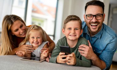 Dijital cihaz teknolojisi aile çevrimiçi eğitim kavramı. Evde dijital cihazları olan mutlu genç bir aile..