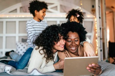 Aile mutluluğu çocuklar eşcinsel ebeveynler konsepti. Mutlu çok ırklı çift evde çocuklarla eğleniyor.