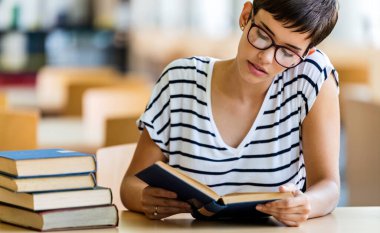 Eğitim kütüphanesi, üniversite eğitimi ve insanların konsepti. Üniversite kütüphanesinde kitap okuyan gülümseyen öğrenci kız.