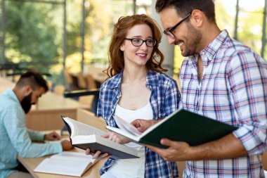 Eğitim kampüsü arkadaşlığı ve insanların konsepti. Bir grup mutlu öğrenci kütüphanede birlikte okuyorlar..