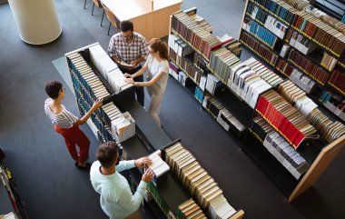 Eğitim kampüsü arkadaşlığı kavramı. Bir grup mutlu öğrenci üniversite kütüphanesinde birlikte öğreniyor.