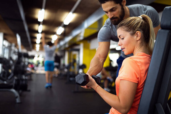 Young beautiful woman doing exercises with personal trainer in gym