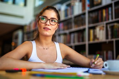 Tired young female studying and preparing for exam in college library. Study education people concept