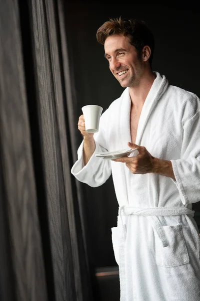 温泉ウェルネスホテルでリラックスしてお茶を飲むバスローブのハンサムな若い男 — ストック写真