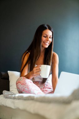 Mutlu genç bir kadın çalışıyor, evde dizüstü bilgisayarla web sörfü yapıyor. İnsanlar, teknoloji, ev kavramı