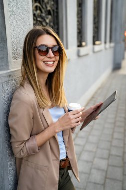 Çekici genç ve başarılı kadın kahve içiyor ve tatilin tadını çıkarırken dijital tablet kullanıyor.