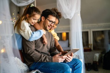 Mutlu bir aile. Baba ve çok ırklı çocuklar evdeki tablette oynuyorlar. Teknoloji, insanlar konsepti
