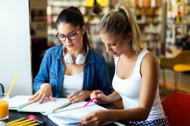 Üniversite kütüphanesinde okuyup sınava hazırlanan mutlu genç arkadaşlar. Eğitim insanları kavramını öğren