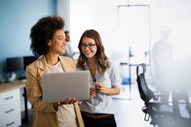 Ofisteki bir dizüstü bilgisayarda birlikte çalışan mutlu, çok ırklı iş kadınları.