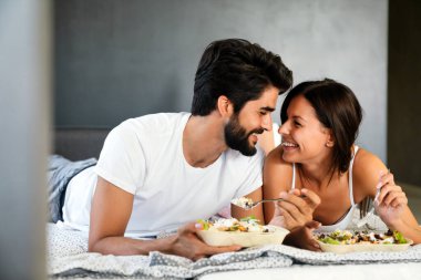 Genç beyaz çift yatakta romantik bir kahvaltı yapıyor..
