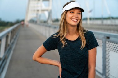 Genç, mutlu, zinde bir kadın şehirde antrenman yaptıktan sonra dinleniyor.