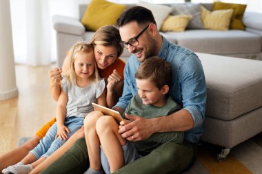 Mutlu genç aile evde eğleniyor. Çocuklu aileler dijital cihaz kullanıyor. Eğitim ebeveynliği mutluluk kavramı.