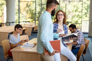 Mutlu genç üniversite öğrencileri ile kütüphane kitaplarında. Bir grup üniversite kitaplığında çok ırklı insan.