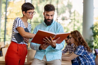 Kütüphanede kitaplarla çalışan mutlu genç üniversite öğrencileri. Üniversitede bir grup çok ırklı insan