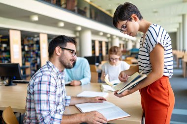 Kütüphanede kitaplarla çalışan mutlu genç üniversite öğrencileri. Üniversitede bir grup çok ırklı insan