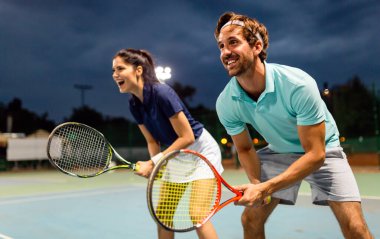 Güzel genç bir çift tenis kortunda bir takım olarak tenis oynuyorlar. İnsanlar spor konsepti