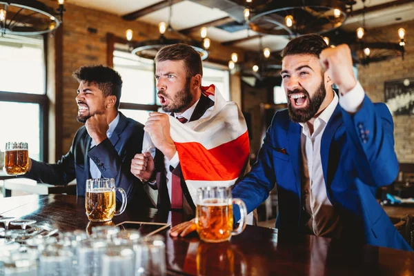 businessmen fans screaming and watching football on TV and drink beer in a pub