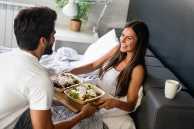 Yatakta rahat ve mutlu bir kadına kahvaltı tepsisi uzatıyorum. Çift, aşk konsepti.